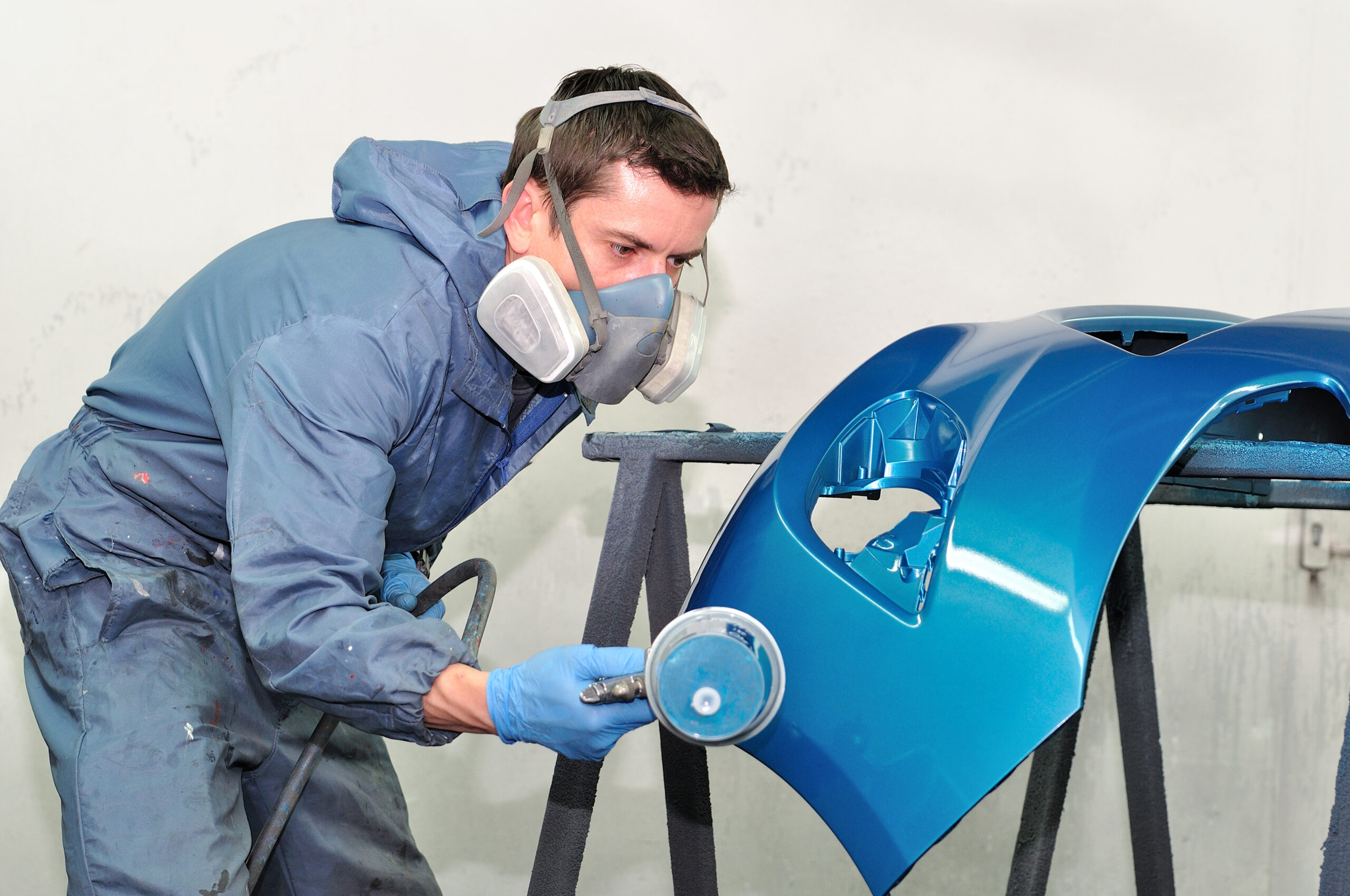 Worker painting blue bumper. bumper repair